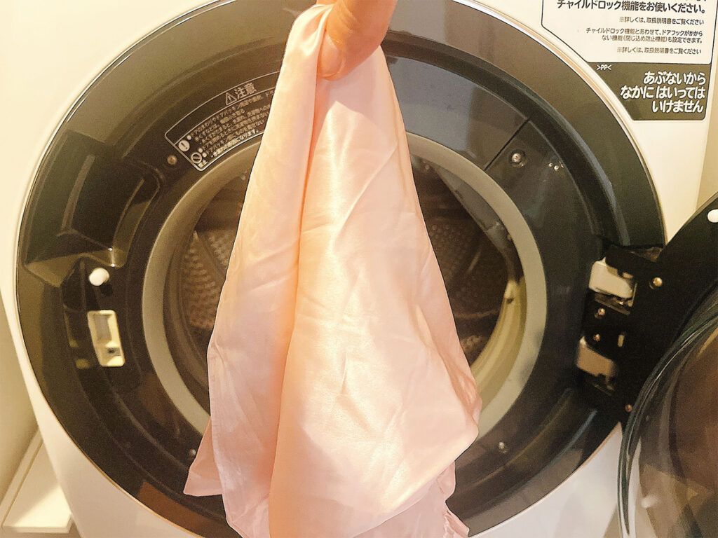 silk pillow cover no effect washing demerit シルク枕カバーのデメリットである洗濯の手間を表現する画像。洗濯ネットに入れたカバーを、少し面倒そうに洗濯機に入れようとしています。