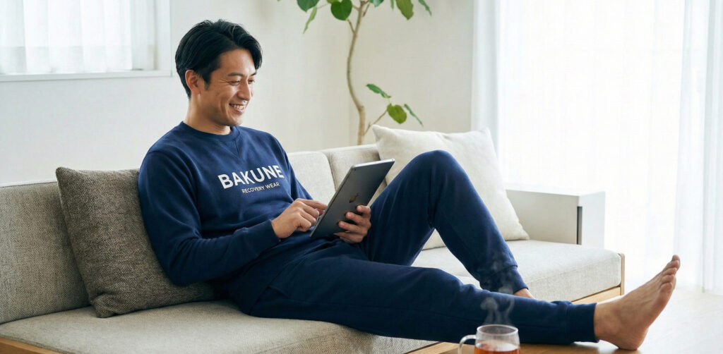 リビングでリラックスしながらリカバリーウェアのスウェットを着用する男性。人気リカバリーウェアを比較し、日常での使いやすさで選ばれる理由を表現。